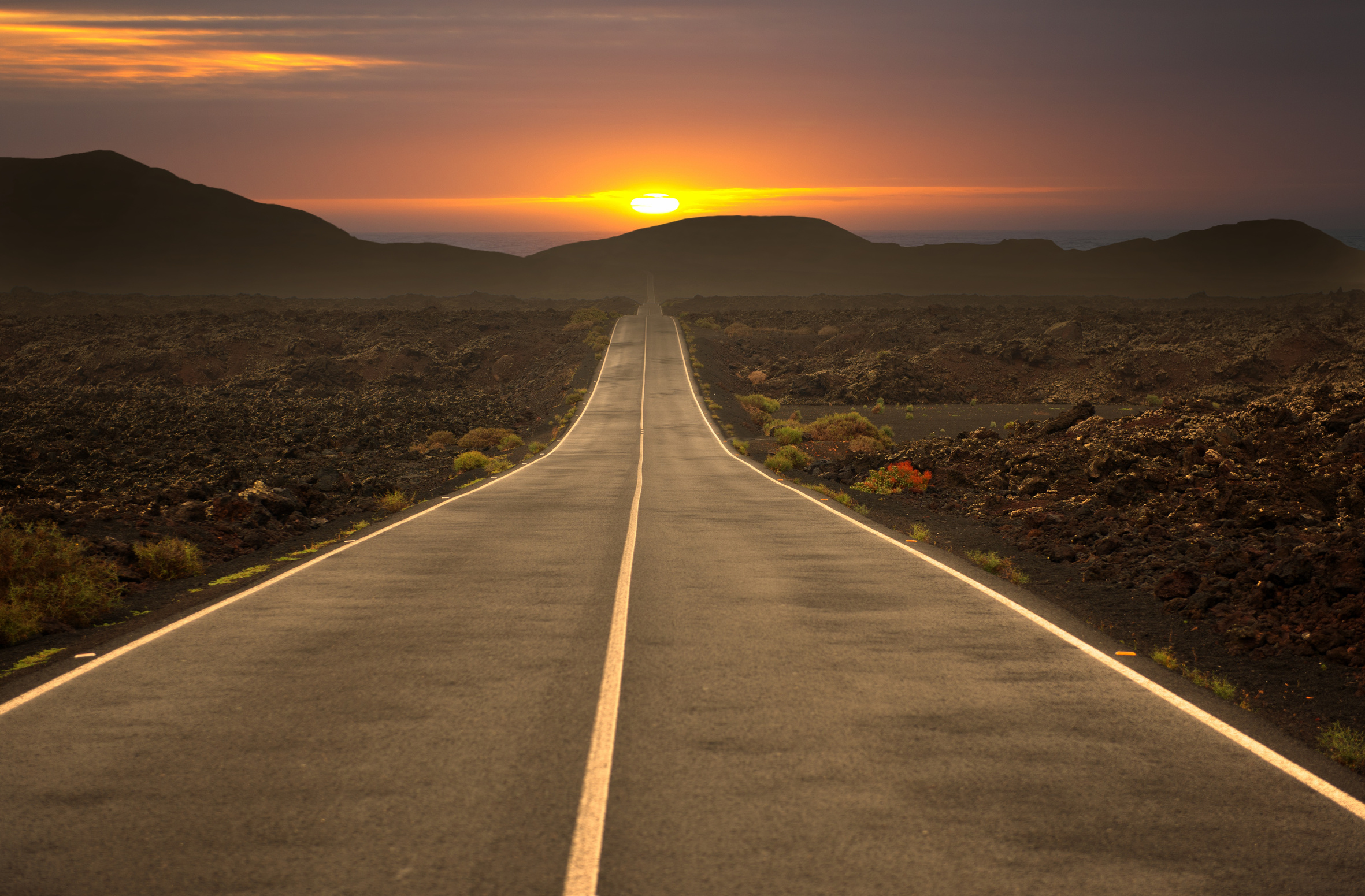 a long road surrounded by mountains leading to a beautiful sunset, showcasing the next travel experience